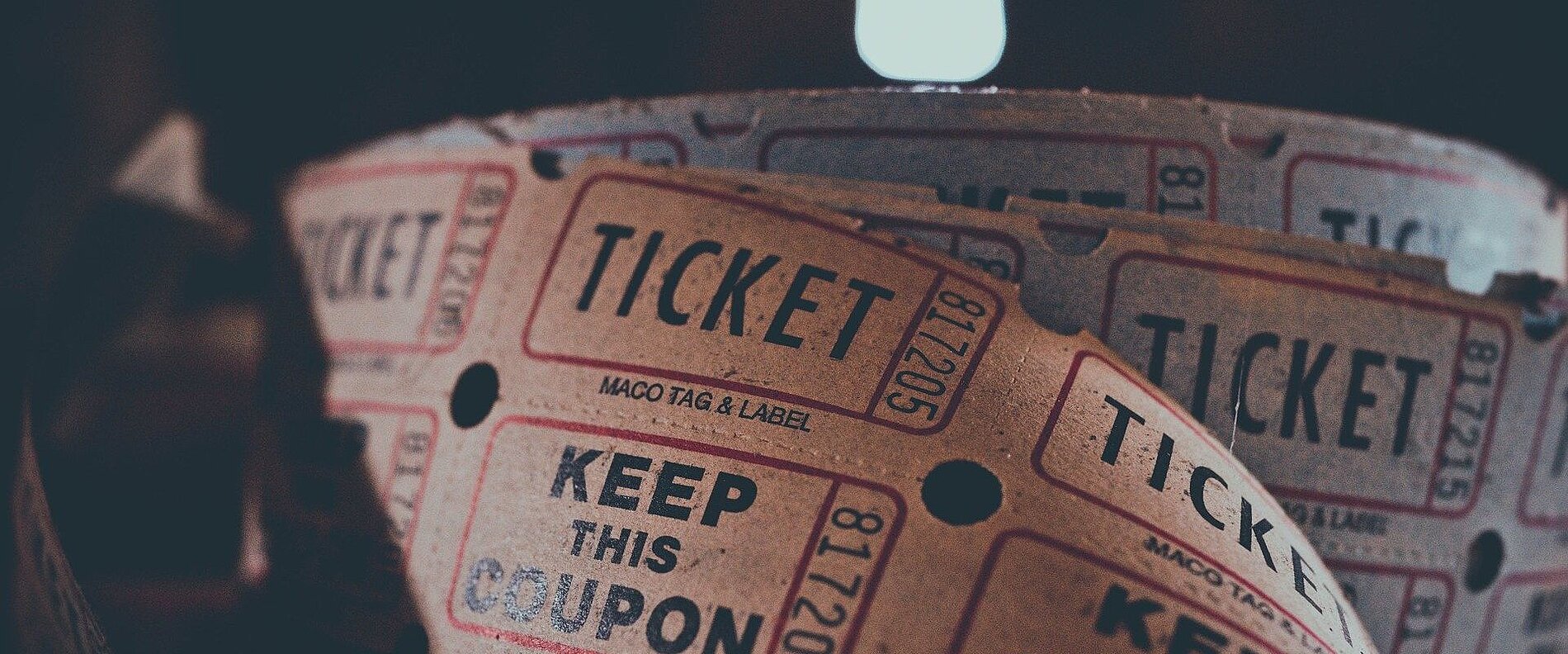 Eine Ansammlung von Eintrittskarten in einer Schüssel. Die Karten sind braun und mit rot-weißen Elementen gestaltet. Auf den Karten steht "TICKET" und "KEEP THIS COUPON".