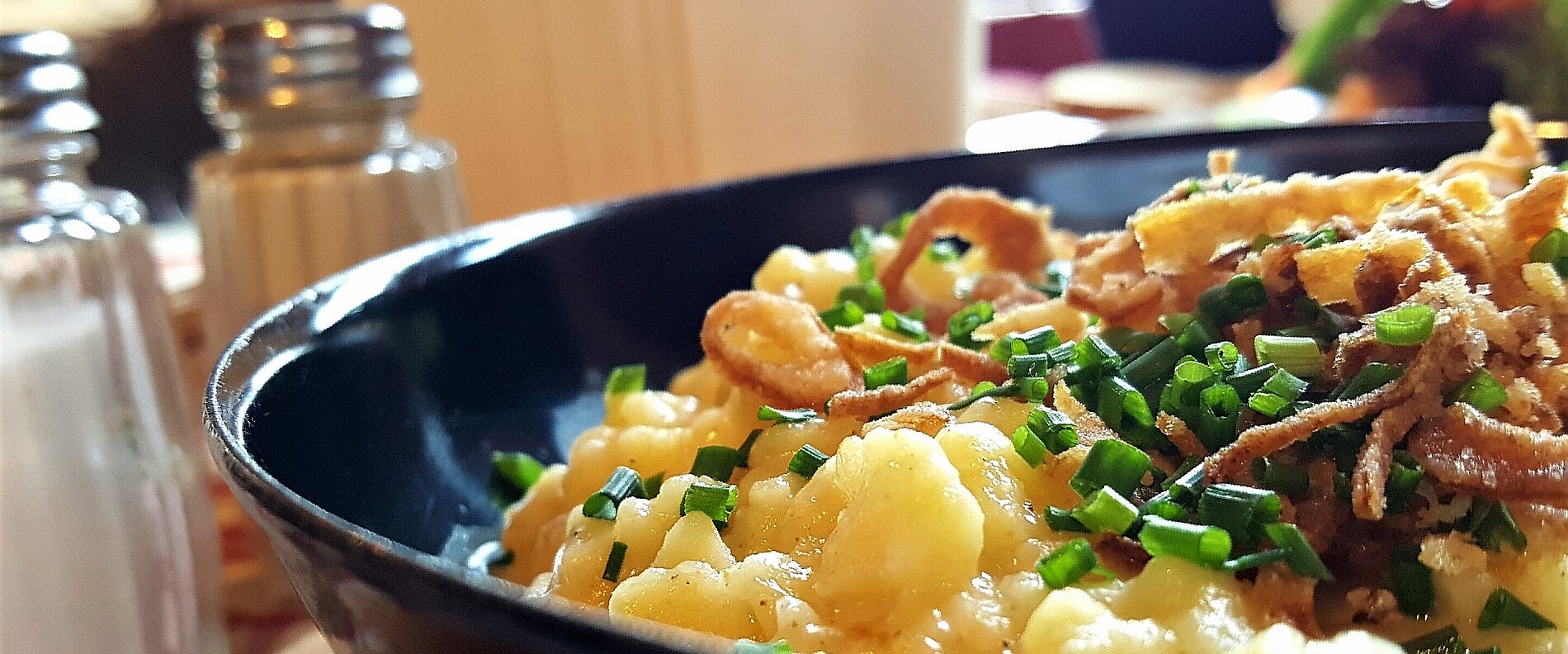 Eine Schüssel mit Reisgericht, garniert mit frischem Schnittlauch und knusprigen Zwiebelringen. Im Hintergrund sind zwei Salz- und Pfefferstreuer zu sehen. Das Gericht wirkt appetitlich und ist gut portioniert.